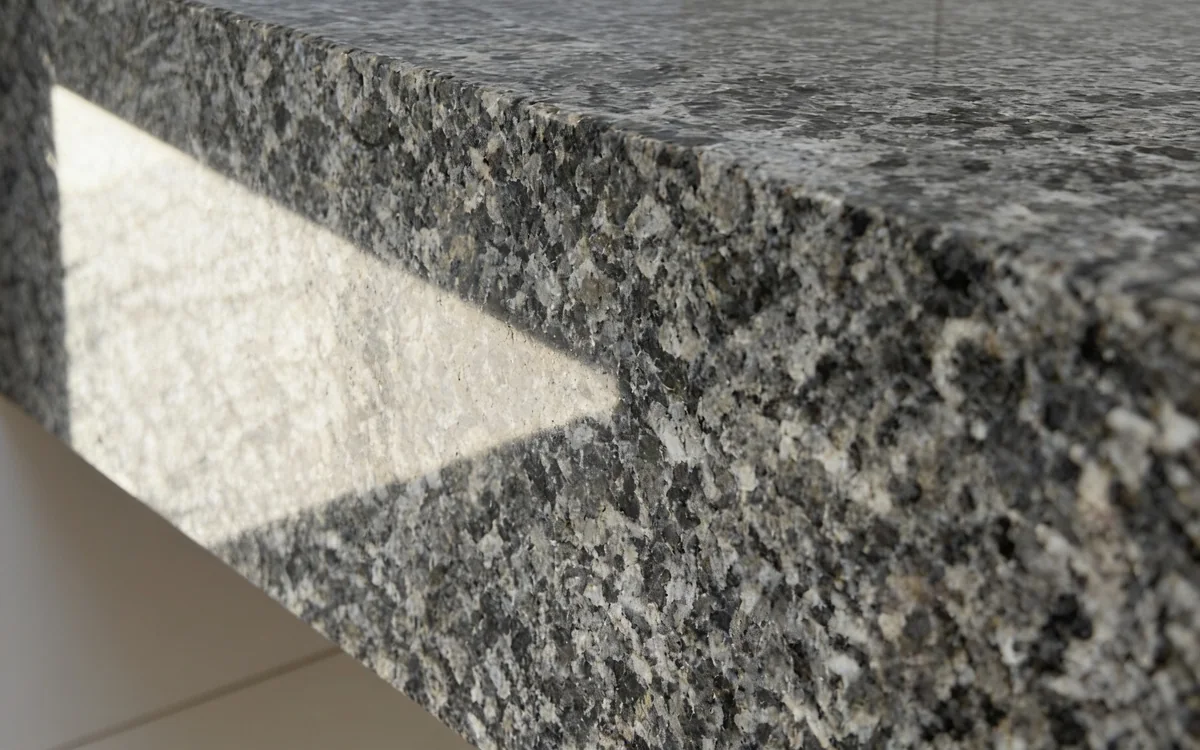 Granito Cinza Ocre polido de perto: cinza de grão miúdo, com pontos pretos, cinza e brancos